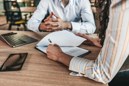 Man and woman sit at a table going over documents using a laptop and a tablet
